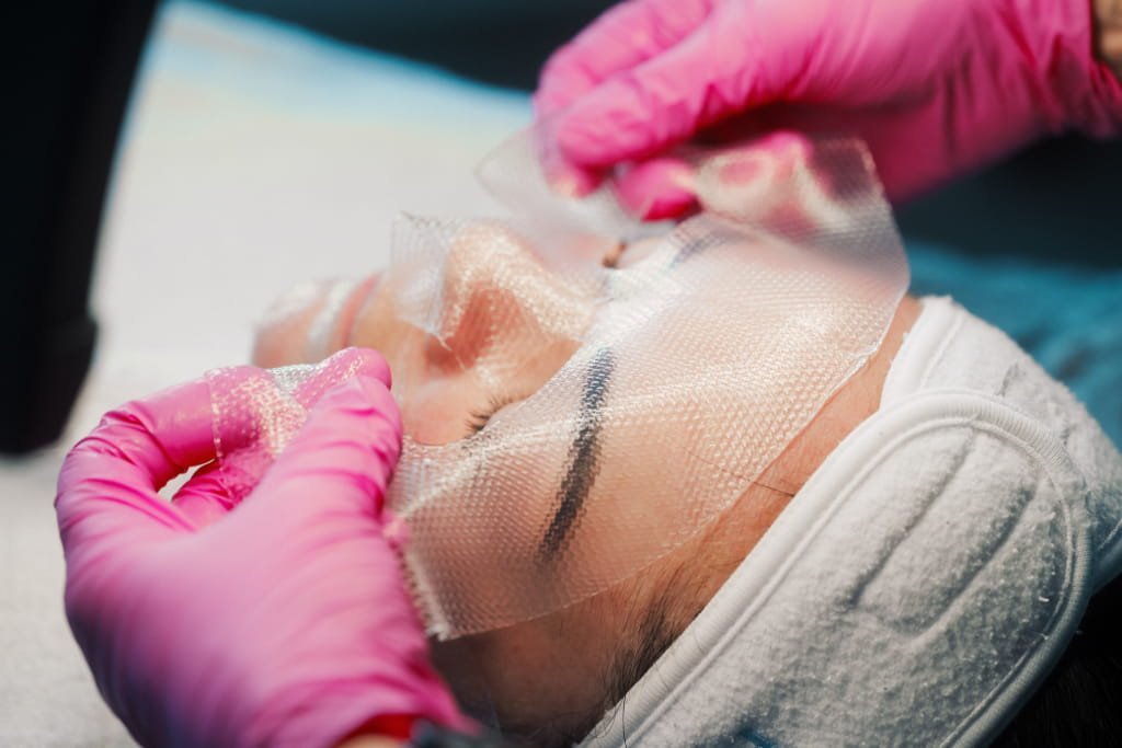 A Skin Therapist at Dr Lauren’s clinic applying a sheet mask to a patient’s face.
